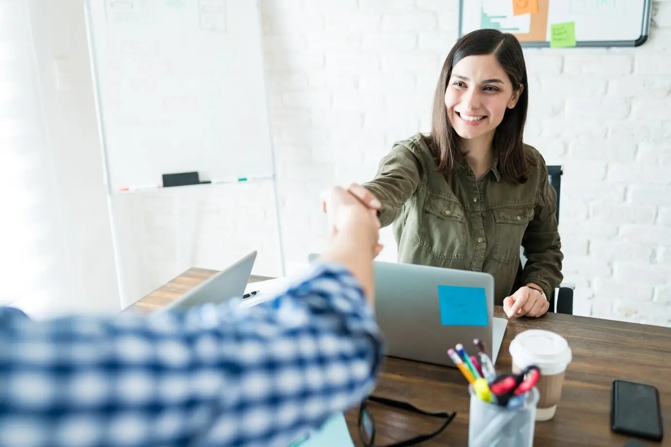 Улыбающаяся деловая женщина пожимает руку коллеге во время офисной встречи.